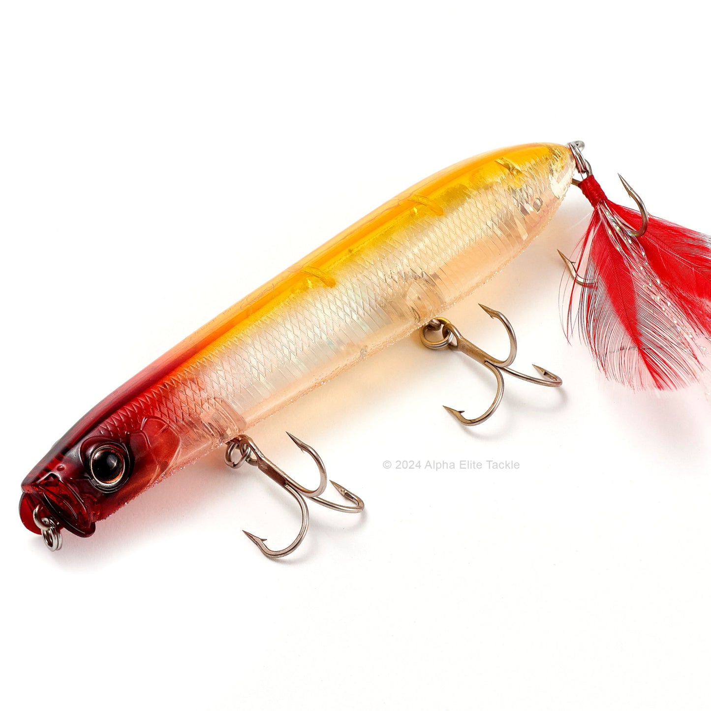 A top water fishing lure with a red and yellow gradient body, three treble hooks, and a red feathered tail, displayed on a white background.